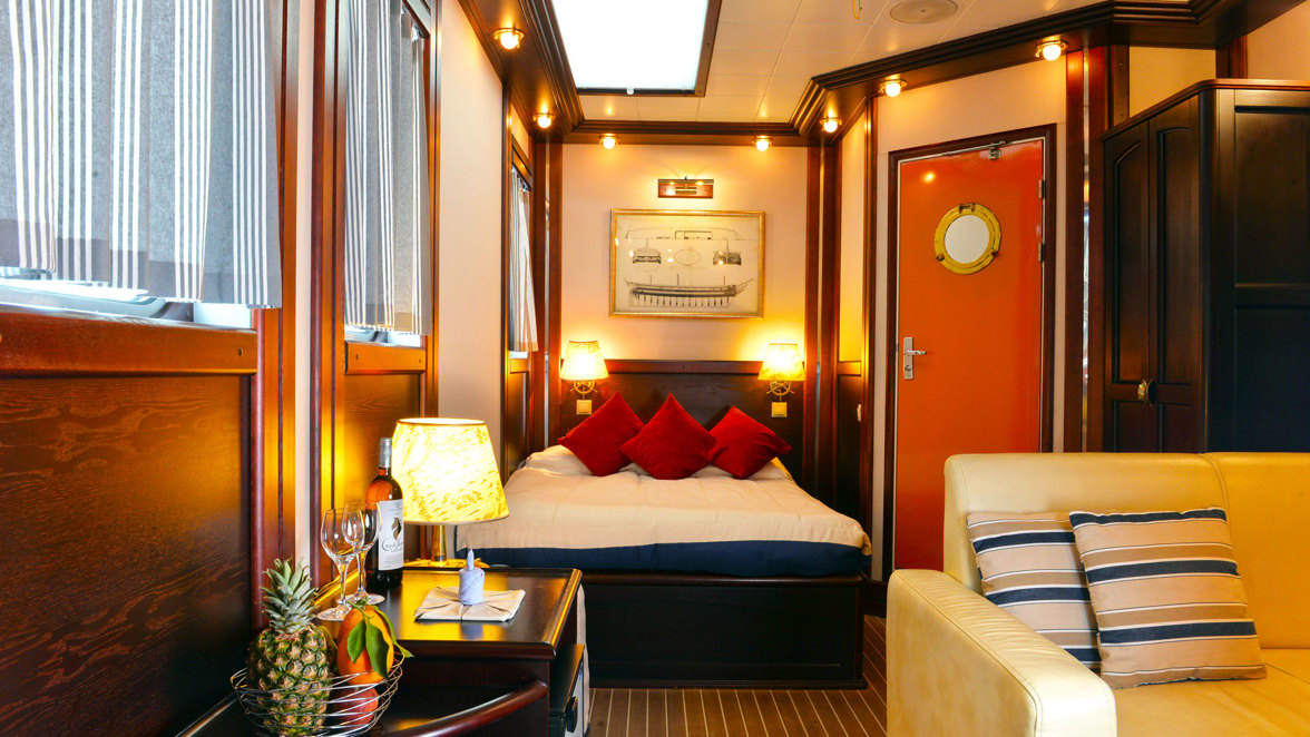 cabin interior with bed and sofa, coffee table, wine and fruits