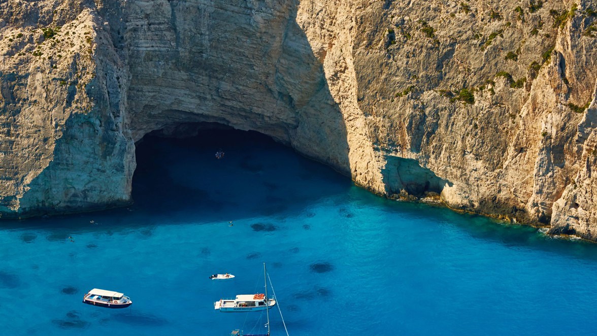 boats next to rocky coast with caves