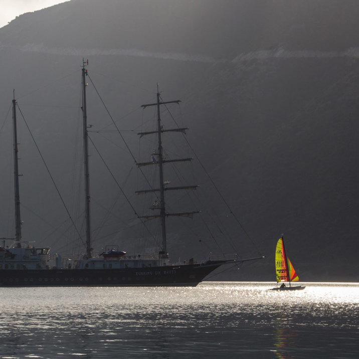 ship in island's shadow next to a boat and windsurfing board