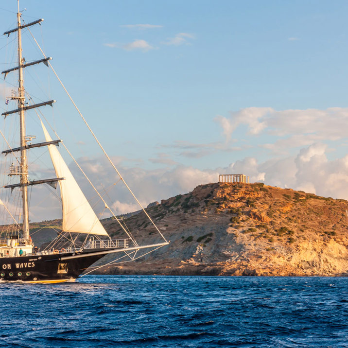 ship next to rocky island with temple ruins on top