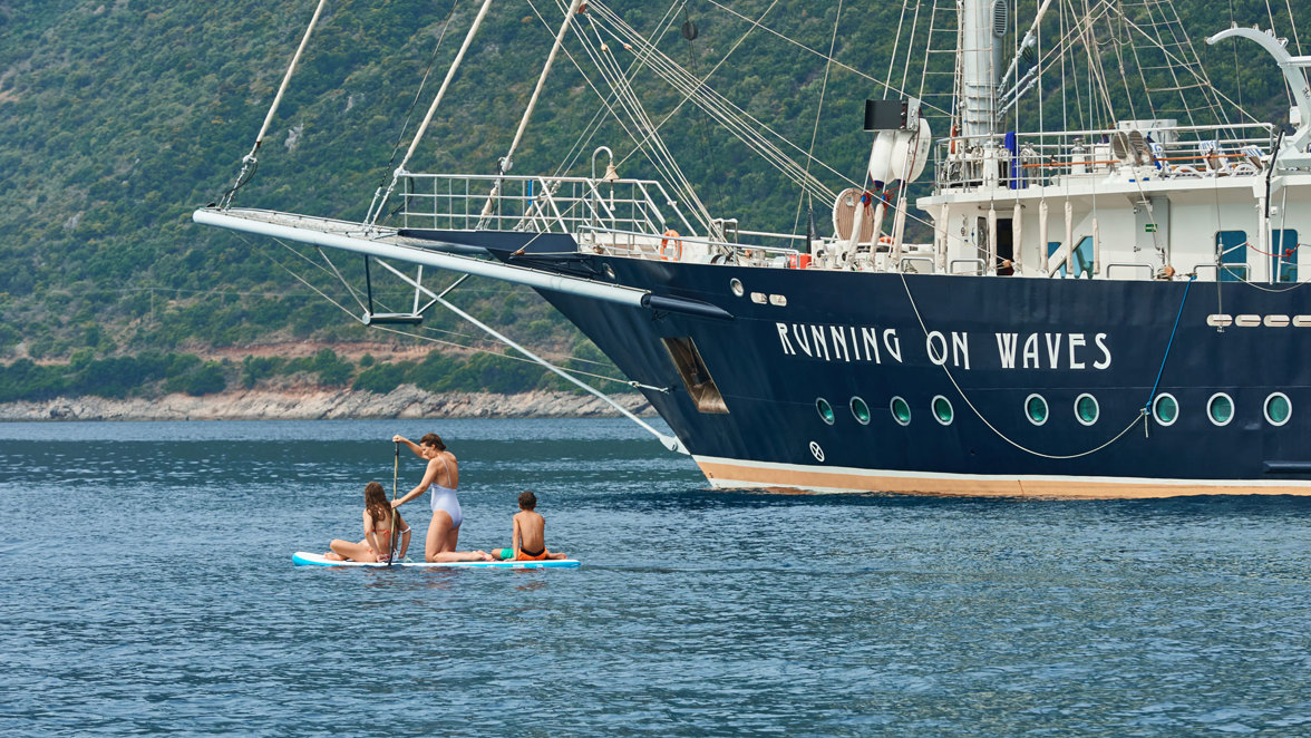 guests swimming on surfboard with a paddle near ship